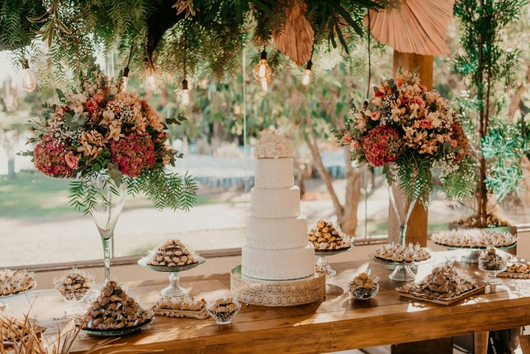 Beautiful outdoor wedding dessert table with floral arrangements and a tiered cake.